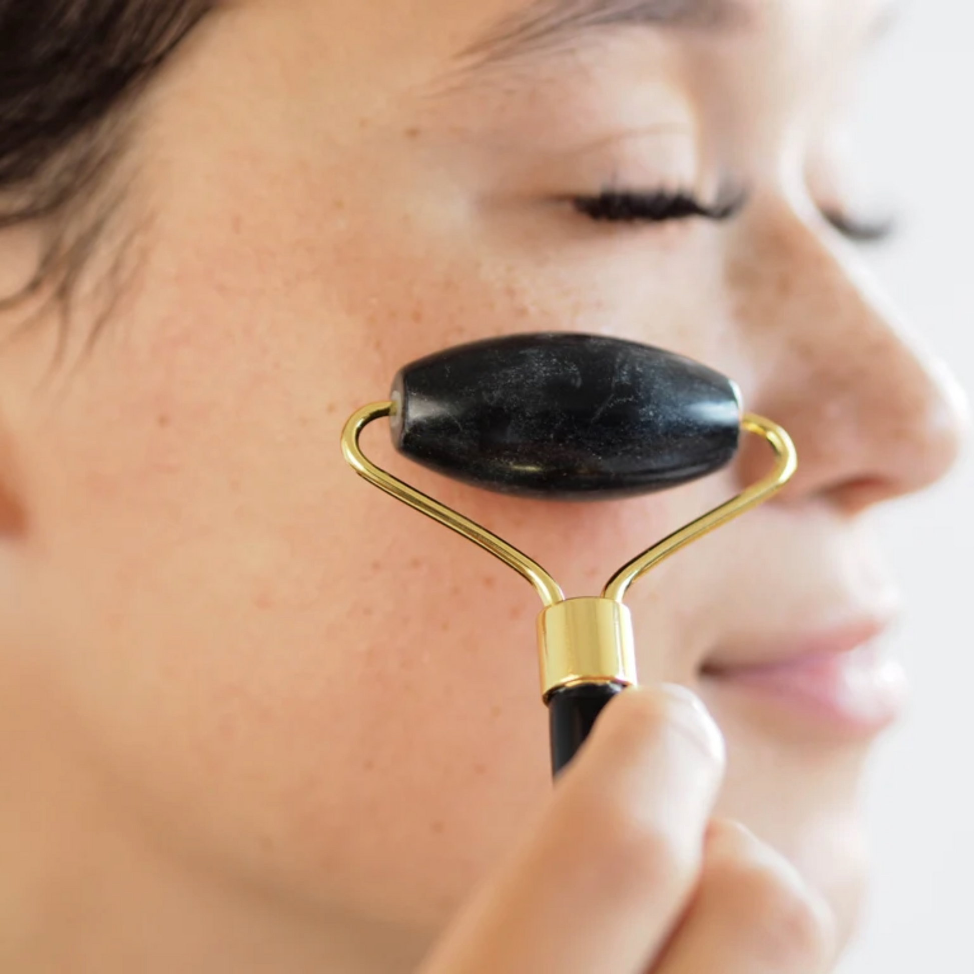 Close up of woman using black jade roller against cheek.