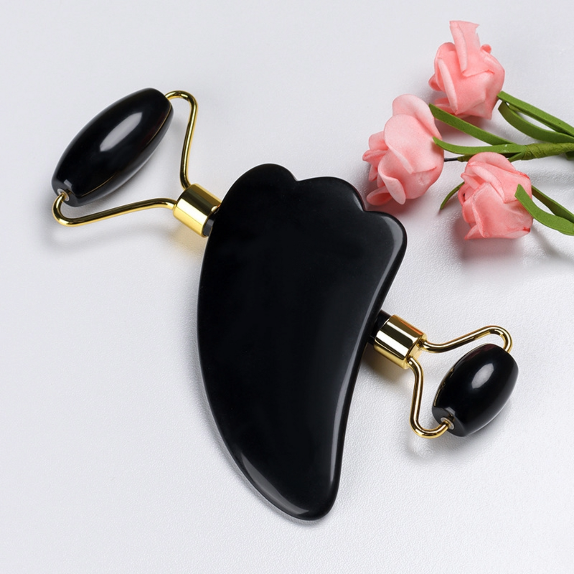 Black Jade Roller with black gua sha next to three pink flowers.