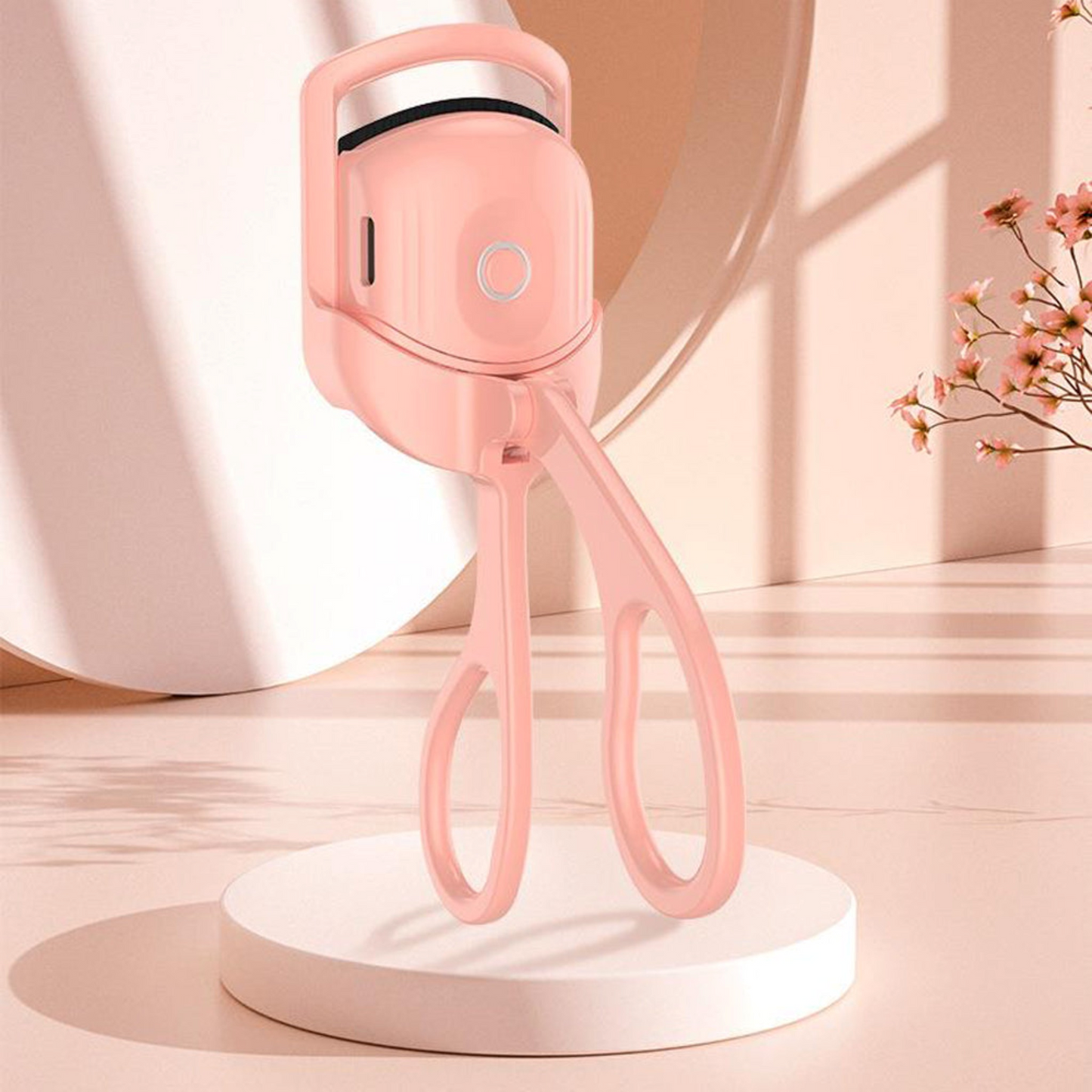 Pink electric heated eyelash curler standing upright on a peach-colored table next to a flower.