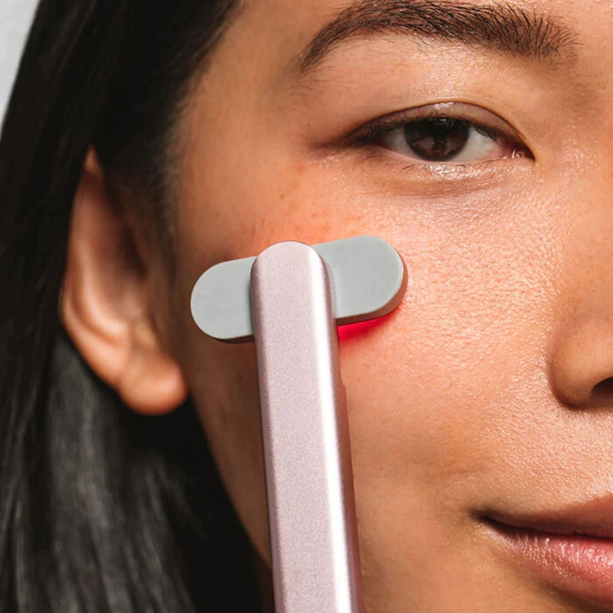 Close up of woman's face with a red light therapy wand pressed against her cheek.