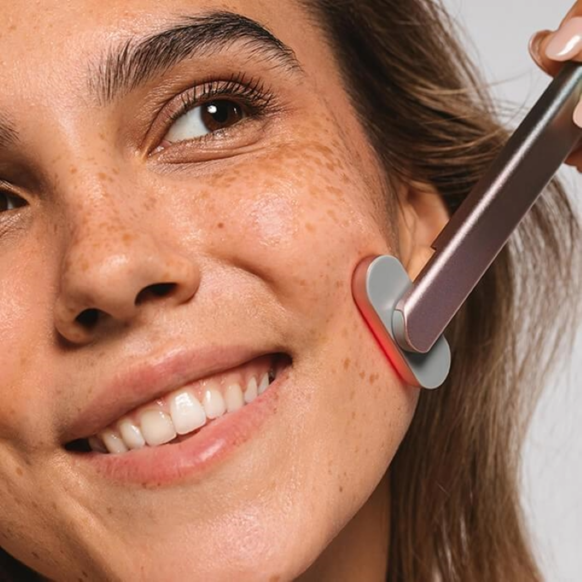 Close up of a woman's face smiling with a Red Light Therapy Wand pressed against her cheek.d 